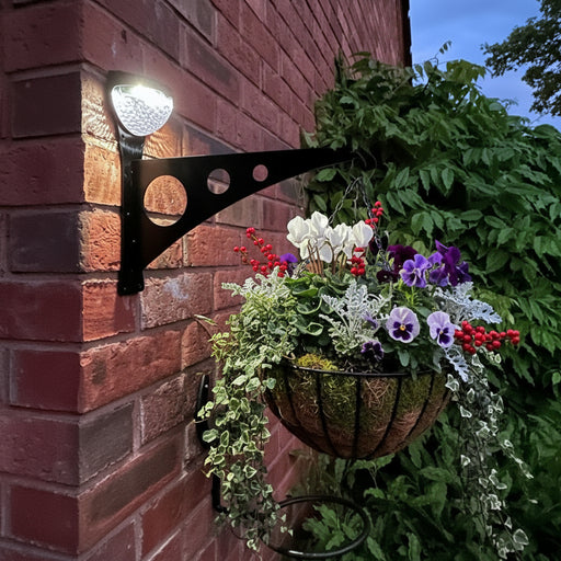 Solar light hanging basket bracket attached to a brick wall with greenery in the background