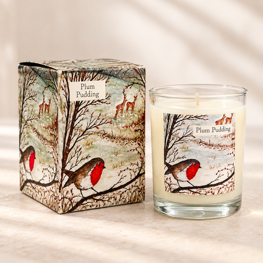 A scented candle in a clear glass jar with cream wax and a winter woodland label, shown next to its matching illustrated box. The label and box feature a robin bird, bare trees, deer, and the text 'Plum Pudding'.